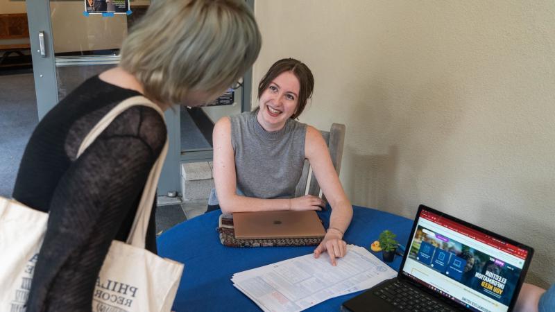 A student sits at a table and talks to a woman